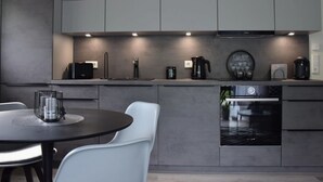 A modern kitchen with grey cabinets, a coffee machine, and a dining area with a table and chairs. - Beach Apartment in Schleswig-holstein (Westerdeichstrich)