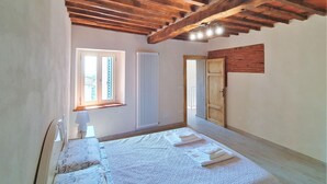 Een slaapkamer met een houten plafond, een raam met zonwering, een radiator en een deur.