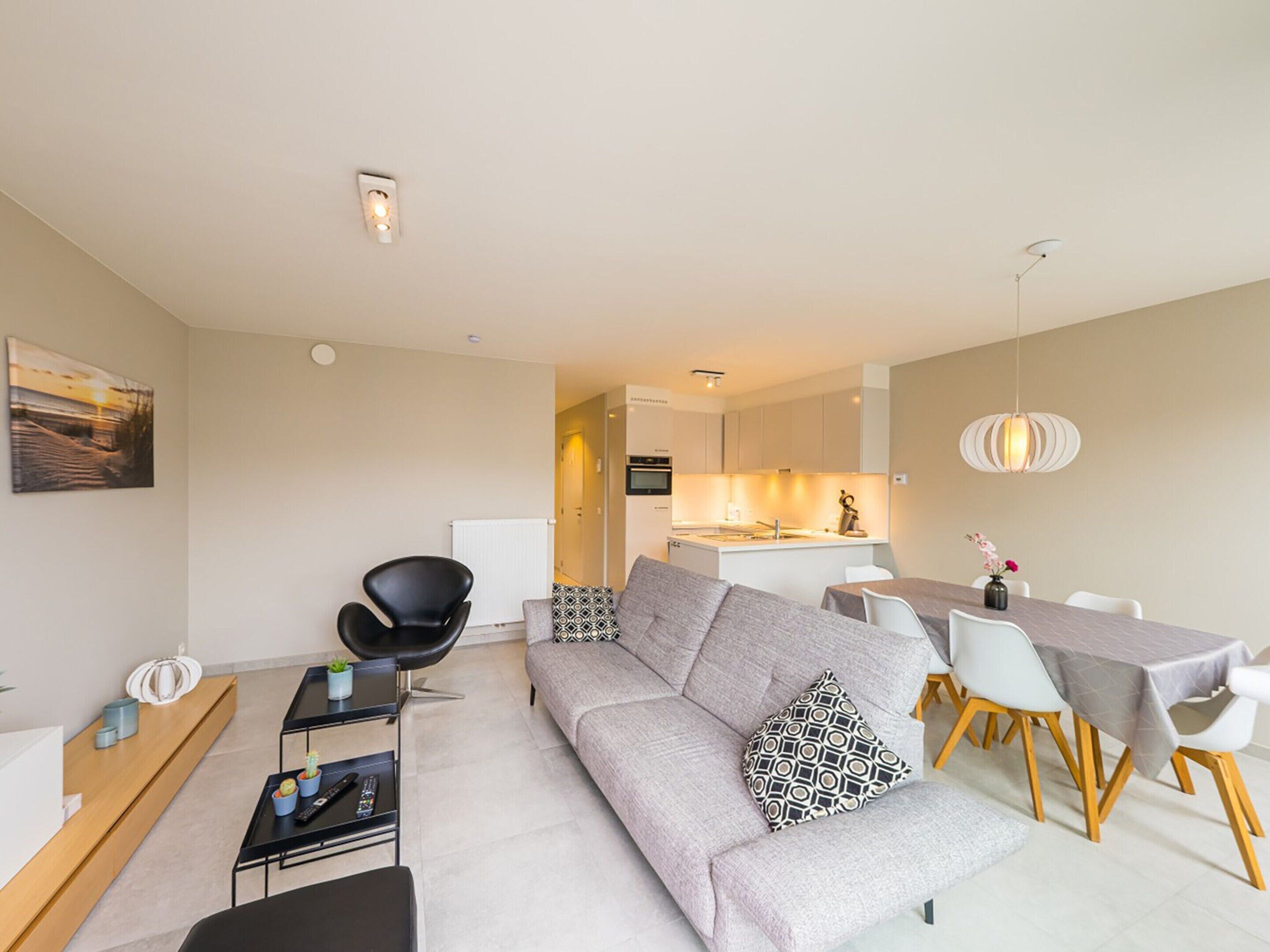 A modern living room with a grey sofa, black chair, and a dining table with white chairs.
