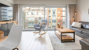 En moderne stue med en grå sofa, en gyngestol, et træbord og et fjernsyn på et skab.