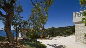 A courtyard with a stone wall, a tree, and a view of the sea. - Brdar Comfortable Holiday Residence (Marina)