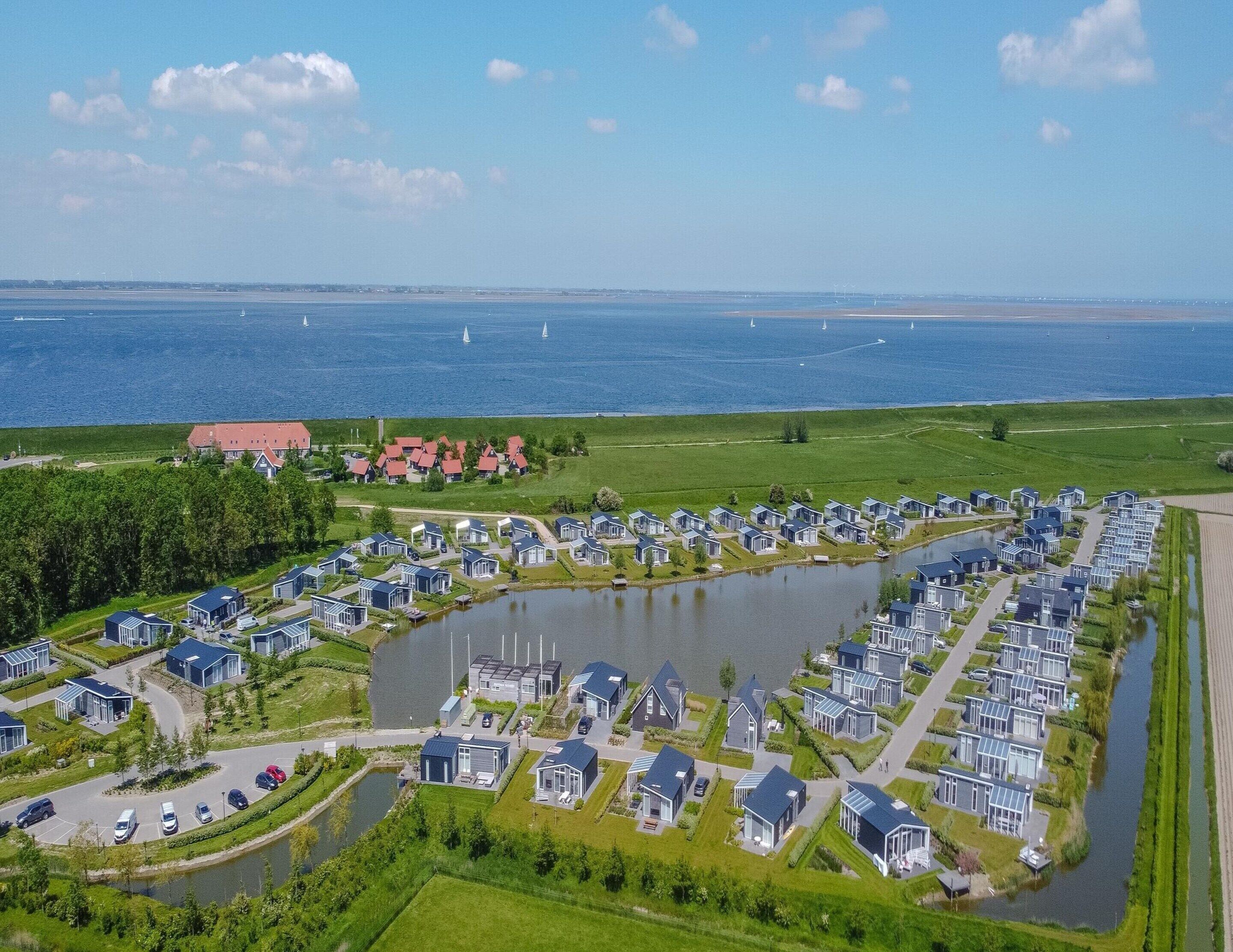 A lakeside residential area with modern houses, a large body of water, and a distant view of the sea with sailboats.