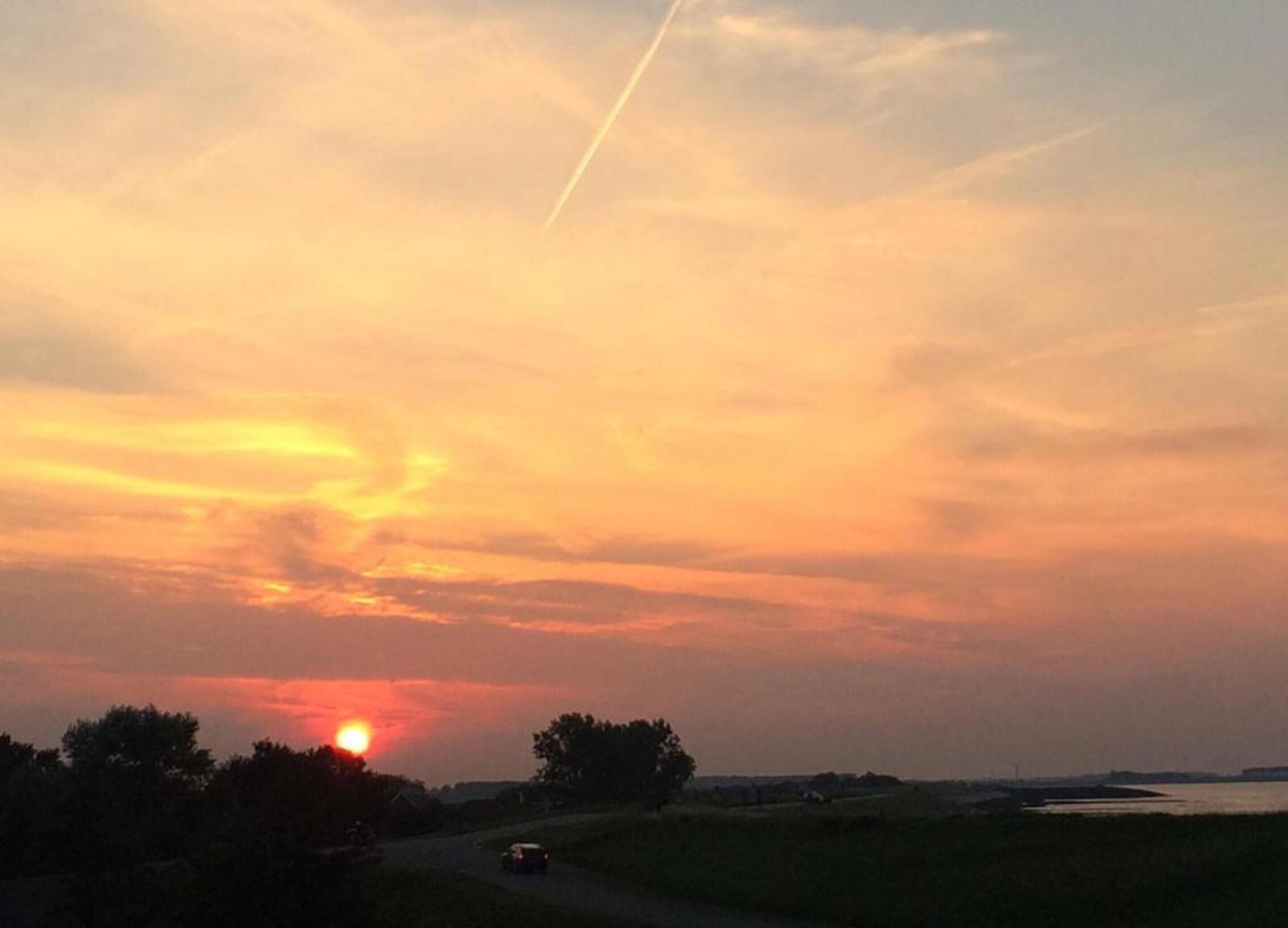 A sunset over a rural landscape with a road and trees.