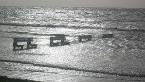Una playa con tres bancos de madera orientados al océano.