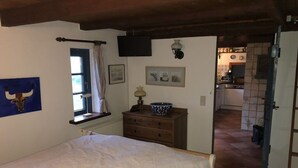 Un dormitorio con cama, ventana con cortinas, lámpara de pared y puerta que da a una cocina.