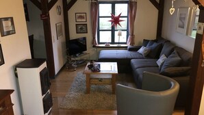 Una sala de estar acogedora con sofá, una mesita de centro y una televisión. Se ve una ventana con cortinas y una decoración con forma de estrella.