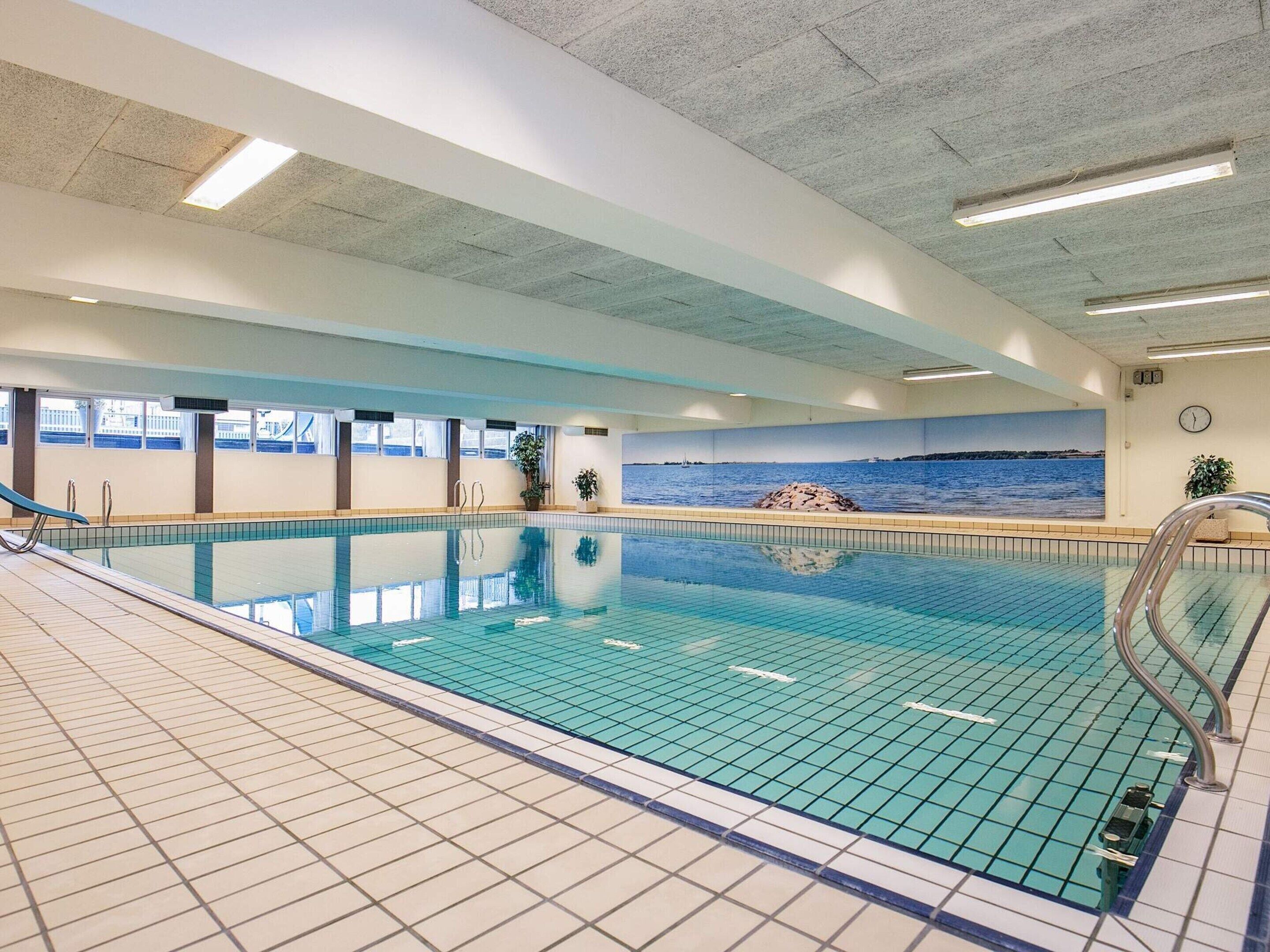 An indoor swimming pool with clear blue water, tiled walls, and a mural of a coastal scene.