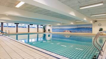 An indoor swimming pool with clear blue water, tiled walls, and a mural of a coastal scene.