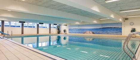An indoor swimming pool with clear blue water, tiled walls, and a mural of a coastal scene.