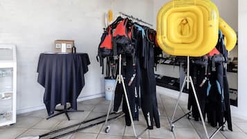 Ein Zimmer mit einem Tisch, der mit einem dunklen Tuch bedeckt ist, einem kleinen Hausmodell und einem Gestell mit schwarzen und roten Jacken.