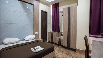A modern hotel room with a large bed, a wooden dresser, a vanity with a mirror, and a desk with a chair.
