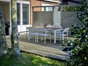 A patio with a wooden deck, white outdoor furniture, and a glass door leading to an interior space. - Christel Modern Retreat (Langeoog)