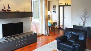 Una sala de estar moderna con chimenea, un sofá de cuero negro, una mesa de centro de madera y un televisor sobre un mueble negro.