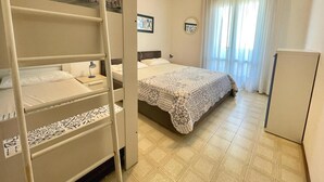 Une chambre avec des lits superposés, un lit simple, une table de chevet avec une lampe, une armoire et une fenêtre avec des rideaux.