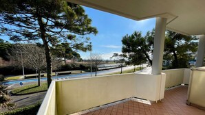 Un balcon avec un sol carrelé, donnant sur une route et bordé d’arbres.