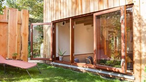 A wooden cabin with large sliding glass doors, a small patio with a chair and potted plants, and a wooden fence in the background. - Holiday Home Ecolodge The Pearl (Schoorl)