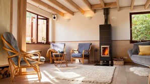 A cozy living room with wooden beams, a fireplace, wicker chairs, and a sofa. - Holiday Home Ecolodge The Pearl (Schoorl)