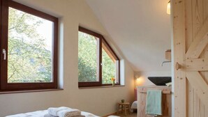 A bedroom with a large bed, two windows, a wooden door, and a small stool. - Holiday Home Ecolodge The Pearl (Schoorl)