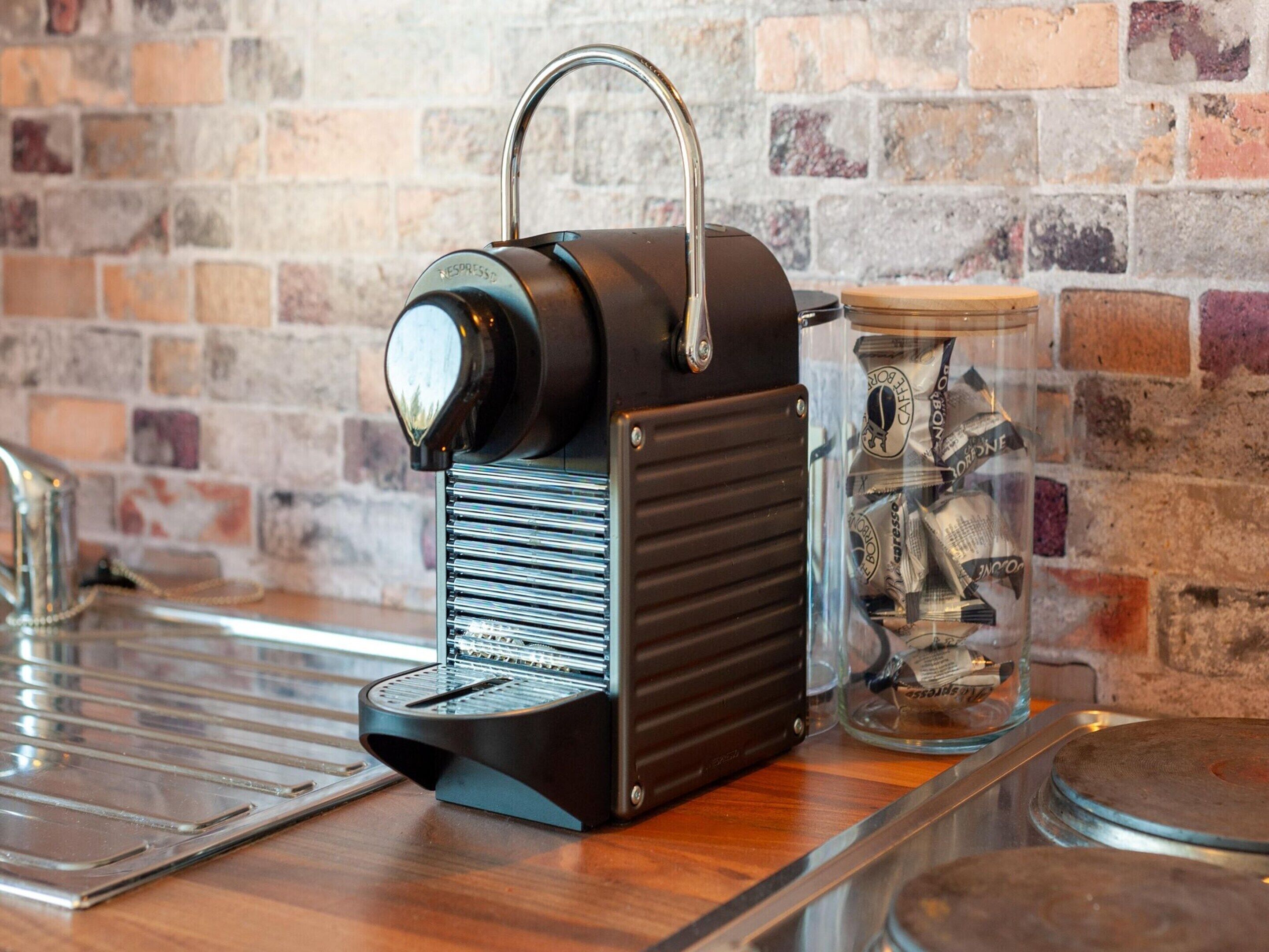 A vintage espresso machine with a metal handle, placed on a wooden counter next to a glass jar filled with coins.