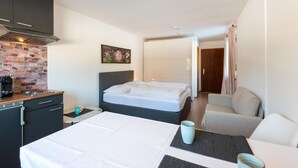 A modern hotel room with a bed, a sofa, a desk with a kettle, and a brick wall. - Idyllic Apartment in Sibratsgfall (Sibratsgfaell)