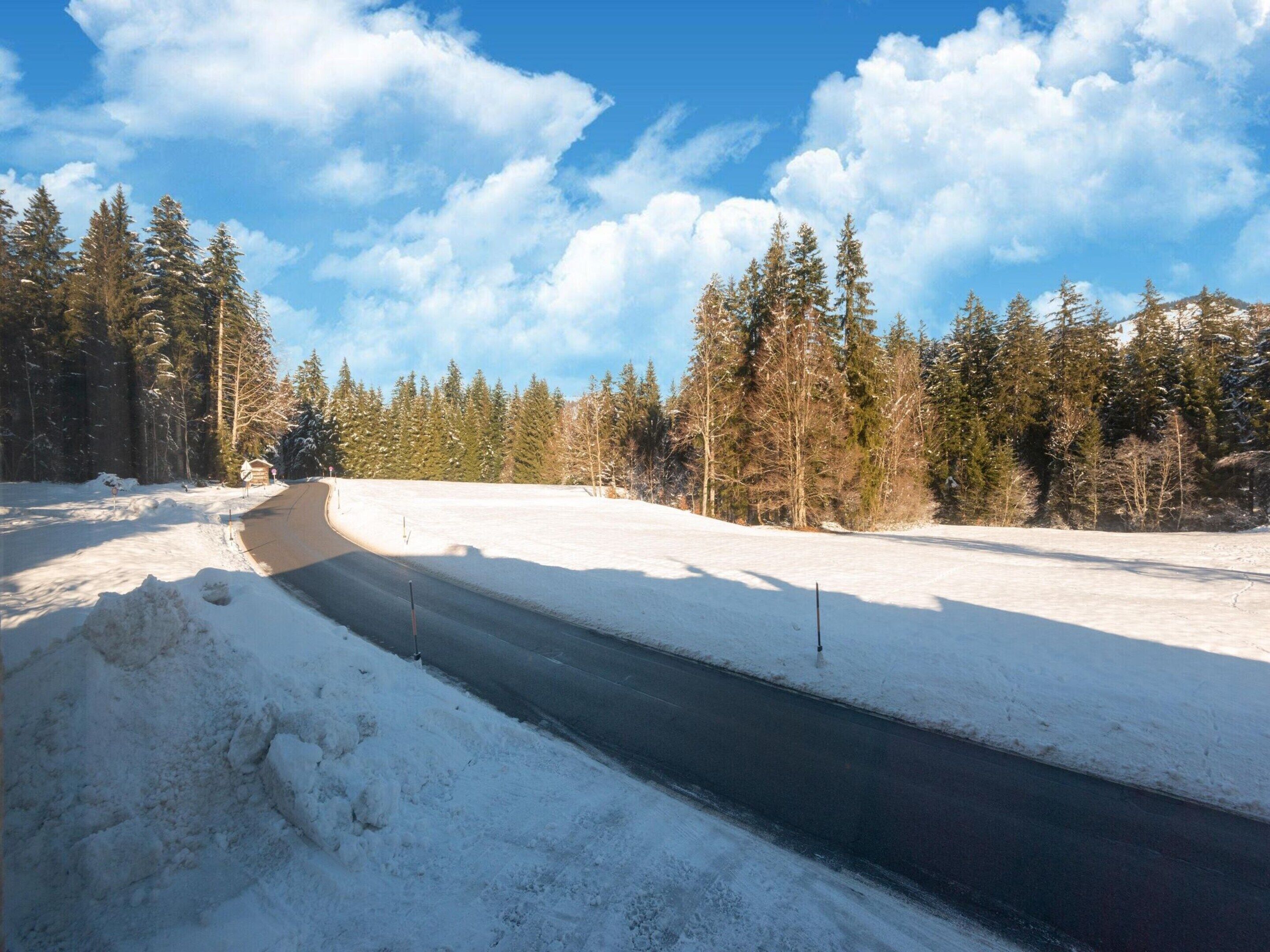 Una strada innevata con cielo sereno e alberi sempreverdi.