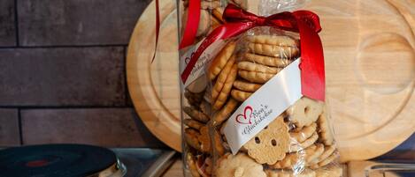Un sac de biscuits, orné d’un ruban rouge et d’un logo en forme de cœur, posé sur une surface en bois, avec une cuisinière en arrière-plan.