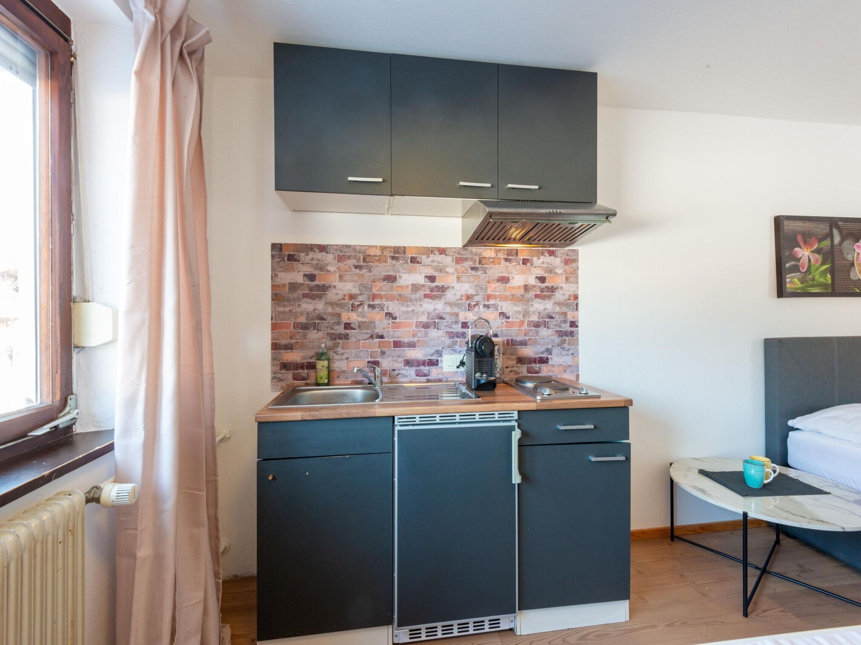 Una cocina compacta con protector contra salpicaduras de ladrillo, armarios oscuros y un pequeño comedor con una mesa y una silla.