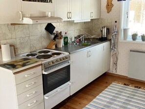Una cocina con armarios blancos, una estufa y una ventana con plantas.