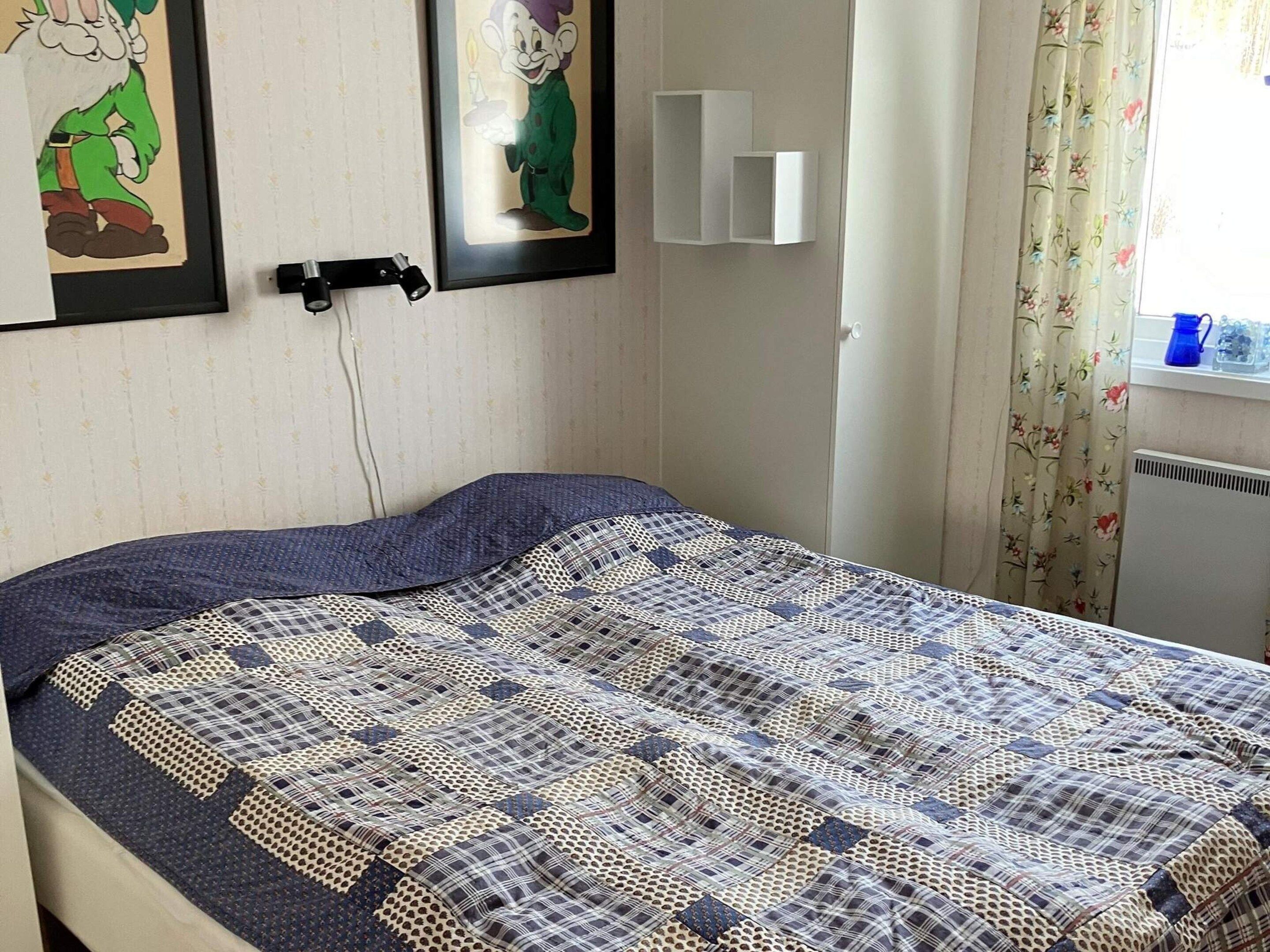 A bed with a patterned quilt, a wall-mounted light, and framed artwork.