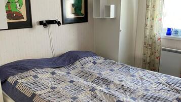 A bed with a patterned quilt, a wall-mounted light, and framed artwork.
