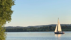 A sailboat on a calm lake with a forested shoreline and hills in the background. - 6 Person Holiday Home in Sunne (Sunne)