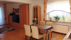 A dining area with a wooden table, chairs, a vase with flowers, and a window with curtains. - Ferienwohnung in Bissendorf (Bissendorf)
