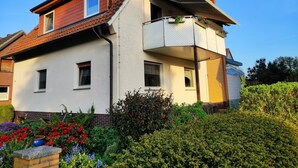 A two-story house with a balcony, a brick chimney, and a garden with various plants and flowers.