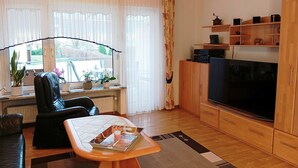 A living room with a sofa, a coffee table with a tray, a TV, wooden cabinets, and a window with curtains.