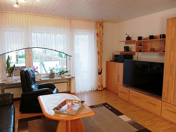 A living room with a sofa, a coffee table with a tray, a TV, wooden cabinets, and a window with curtains. - Ferienwohnung in Bissendorf (Bissendorf)