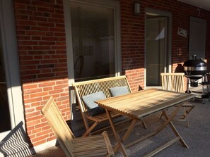 A patio with a wooden table and benches, a barbecue grill, and a large window. - Lange Eins Comfortable Holiday Residence (Arnis)