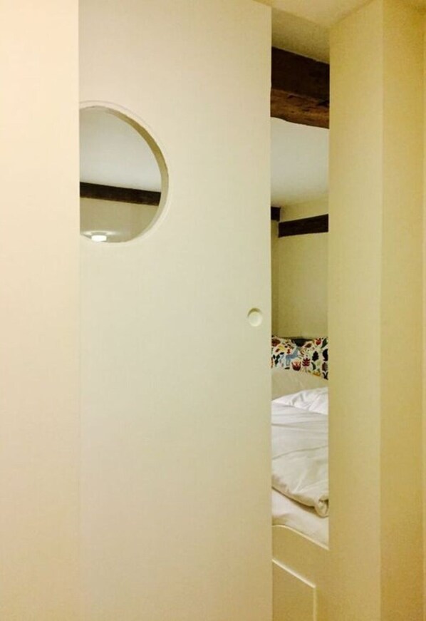 Une pièce avec un lit, un miroir rond accroché au mur et un plafond avec des poutres en bois.