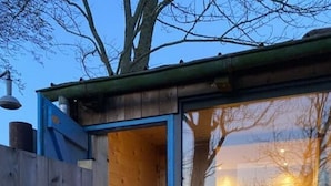 A wooden cabin with a glass door leading to a furnished interior, including a table and chairs. - Holidays in Happiness (Tetenbüll)