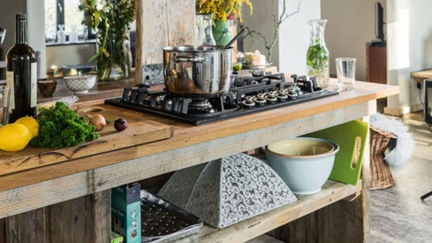 A kitchen with a central island, wooden beams, a stainless steel range hood, and various kitchen items. - Holidays in Happiness (Tetenbüll)