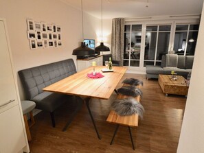 A modern living room with a wooden dining table, grey sofa, and a bench with a fluffy dog.
