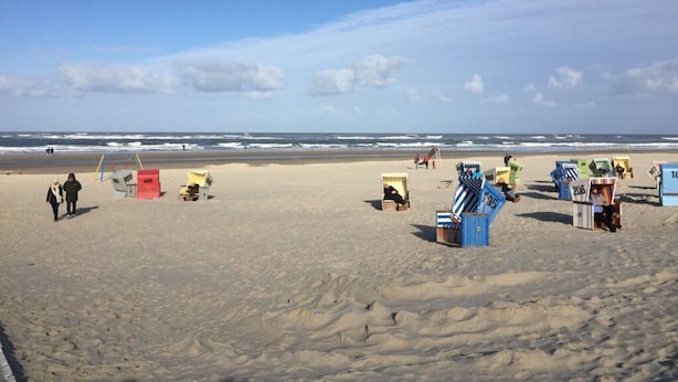 En strand med sand, få mennesker og farverige strandhuse.