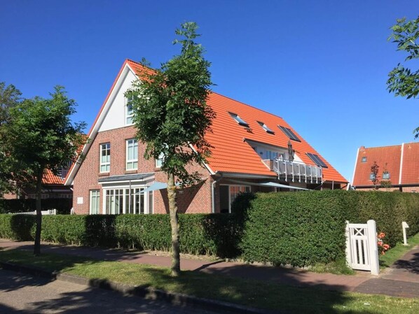 A two-story house with a red-tiled roof, a small balcony, and a white gate.