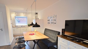 Et moderne køkken med spiseplads, TV og et hvidt skab med skuffer.