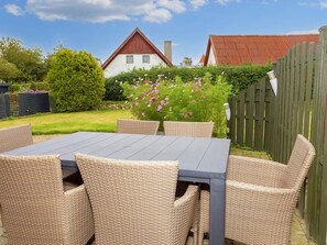 A patio with a table and wicker chairs, surrounded by a garden with flowers and a wooden fence. - 8 Person Holiday Home in Oster Assels (Øster Assels)
