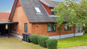 Una casa a due piani in mattoni con tetto spiovente, un portico coperto e un piccolo giardino con arbusti.