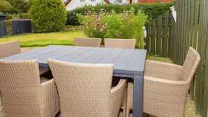 Un patio con tavolo e sedie in vimini, circondato da un giardino fiorito e una recinzione in legno.