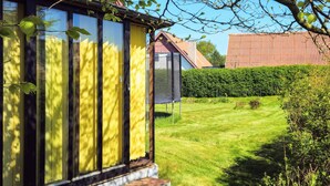 Una casa con ampie finestre, un giardino visibile e una struttura con tetto rosso sullo sfondo.