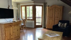 A spacious living area with wooden furniture, a television, and a large window providing natural light. - Huis Hochfirst Appartement 20 (Titisee-Neustadt)