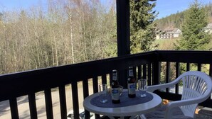A balcony with a round table and two white chairs, overlooking a road and trees. - Huis Hochfirst Appartement 20 (Titisee-Neustadt)
