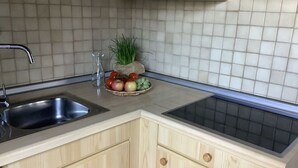 A kitchen with a stainless steel sink, wooden cabinets, a tiled backsplash, and a fruit bowl with apples and tomatoes. - Huis Hochfirst Appartement 20 (Titisee-Neustadt)